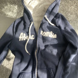 Abercrombie Zip hoodie - Marinblå zip hoodie från abercrombie and fitch med en supermjukt vit innandöme💘       Storlek S - men skulle säga att den passar som en xs/s.🧵   Nypriss är runt 600kr men den säljs inte längre.  Pris kan diskuteras:)💞