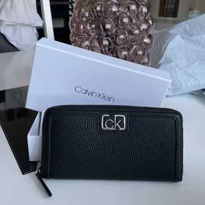 Calvin Klein plånbok  - Säljer en Calvin Klein plånbok där man får plats med mycket, även telefonen. Säljer pga att den inte kommer till användning. Har använts en gång endast och är i helt nytt skick. Nypris 1179 kr.