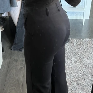 Svarta kostymbyxor  - Säljer dessa kostymbyxor som sitter otroligt snyggt på och är långa i benen. I bra skick förutom knappen som är sönder men det finns också en metallgrej så det är inget som påverkar hur dem sitter eller så. Sitter perfekt i benen på mig som är 175cm lång.