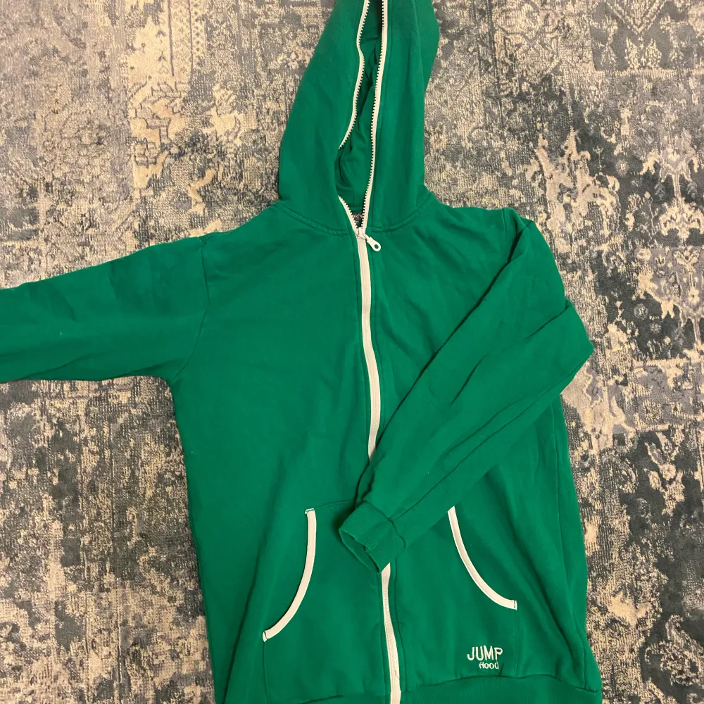 En grön zip up hoodie med vita detaljer, lite kortare model i armarna. Hoodies.