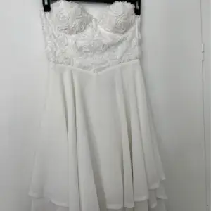 En jätte fin vit klänning med blomdetaljer vid brösten. Endast använd 1 gång. Stl: S Size: 10 Köparen står alltid för frakten 