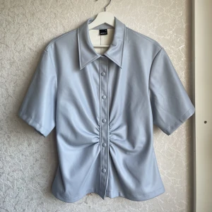 Unik topp med skinnimitation - Ljusblå figursydd topp från Gina Tricot i storlek 42. Den sitter bekvämt och snyggt in mot kroppen och formar sig bra. Skönt material på insidan.  [Kan skicka paket & Mötas upp] (Samfrakt i 3dagar: om du vill köpa något mer av mig fraktas det tillsammans)