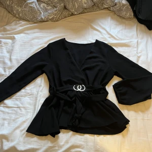 Svart blus med guldspänne i midjan - En väldigt fin, svart blus med guldspänne i midjan och snöre du kan knyta baktill! Den är i väldigt bra skick då den knappast är använd. 