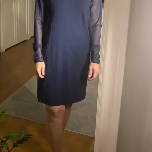 Marinblå klänning med ett tunnare tyg längs armarna. Klänningen är från Gant