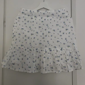 Blommig kjol från NA-KD - Kort kjol med volang & dragkedja på sidan. Säljer på grund av för liten. Aldrig använd, endast provad. Köpte för 299 kr. Frakt tillkommer!