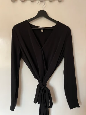 Blus  - Svart blus i härligt material och knyte i midjan. Väldigt gott skick, knappt använd.