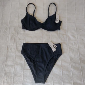 Oanvänd Cubus Riba Swim - svart ribbad bikini - högmidjade trosor och bygelbh - Svart ribbad bikini från Cubus. Riba Swim Wirebra och Riba Swim HL HW Brief. Oanvända med tags kvar. Så snygg helsvart, klassisk modell. Storlek S på överdelen, XS på underdelen. Trosorna finns kvar på webbsidan (199 kr) men bikinitoppen verkar vara slut.