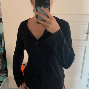 Långärmad tröja  - En svart långärmad tröja med knappar vid halsen. 