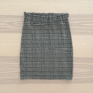 Rutig kjol med räfflad midja - Rutig kjol i svart, vitt och lite mörkgrönt med fin detalj i midjan 🖤Stretchigt tyg och en tight passform. Köpt för länge sedan men bara använd ett fåtal gånger och fortfarande i jättebra skick! Material: polyester, viskos och elastan.