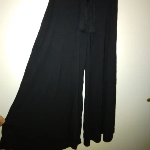 Svarta vida kortare byxor i jersey/mjuk bomull, sk culottes. Oanvända. Felfria. Strlk: 34/XS. - Svarta vida kortare byxor, sk culottes, i jersey/mjuk bomull. Knytband I midjan.  Oanvända. Felfria. Strlk: 34/XS.