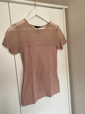 Topp - Lite finare vardagstopp från H&M från den vanliga avdelningen så inte liten small. I blekrosa färg. Färgen är som på närbilden i verkligheten. I stretchigt t-shirt material med överdelen i mesh med spetskant. I gott skick och nytvättad. 