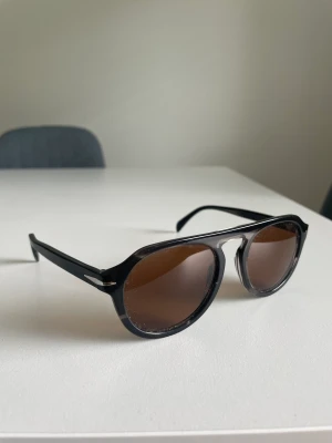 David beckham solglasögon  - Säljer nu ett par david beckham solglasögon. Modell 7009/s storlek L, säljes med tillhörande fodral. Mycket fint skick.
