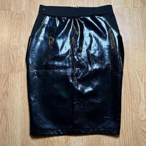 Sexig lackkjol Pinup Fetisch Party Fest Rock Rockabilly Metal - Sexig och elegant kjol med framsida av lack och baksida av stretchig bomull. Klassisk pennmodell. Mycket fint begagnat skick. Längd 55 cm, midja 70, höft 87. Praktiska fickor. Dragkedja bak. Stl 36-38. Bekväm. Allround.