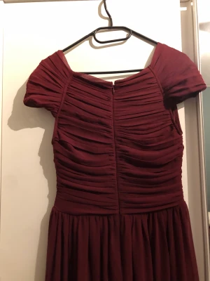 Balklänning - Säljer denna vinröda klänning, från NLY eve, använd enbart en gång. Är i gott skick, maxiklänning, och som ni ser på bilderna har den omlott design framtill och baktill. Har dragkedja baktill. Är utan ärmar. 
