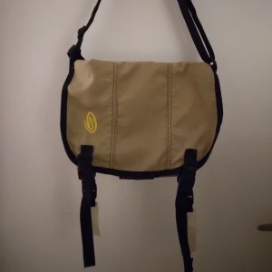 Vintage / retro äkta 1900-tals Timbuk2 messenger bag/ budväska / väska. Nyskick - Retro / vintage äkta 1900-tals Timbuk2 väska / messenger bag / budväska. Beige, guld. Nyskick, hel & ren. Ca 5-6 st fack inuti. Går att tvätta i maskin i skonsamt program utan sköljmedel. Reflexer ingår, midjeband saknas. 40 cm hög, 30 cm bred, 15 cm djup