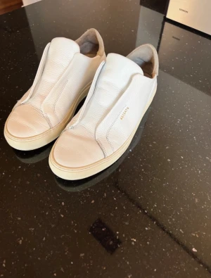 Axel Arigato skor - Ett par snygga vita Axel Arigato skor i läder, storlek 42. Sparsamt använda. Box medföljer. Skriv om ni har fler frågor 