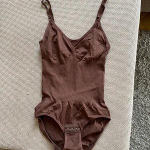 Lillyshape bodysuit brun - Helt ny brun bodysuit i storlek S från Lilyshape som säljs för jag ville endast testa! Superskönt material, kramande midja och lätta haspar i grenen.  Produkten är endast öppnad och kommer hem till dig i sin orginalförpackning!