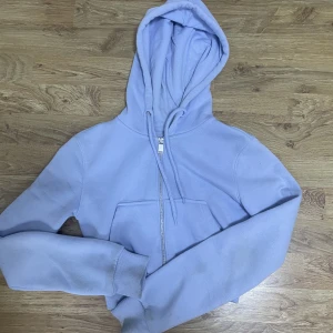 Ljusblå kofta - Ljusblå kroppad huvtröja med dragkedja och luva.