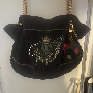 Juicy Couture Väska - Säljer min fina äkta juicy couture väska då jag köpt en ny! Bra skick och även små fack man kan lägga saker i. Smutset i väskan på bild 2 har blivit borttaget! Rosetten har jag satt på från min parfym då det såg finare ut enligt mig men den går att ta av❣️