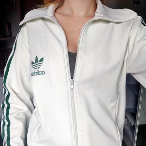 Adidas jacka - En vit Adidas jacka med mörkgröna ränder 💕 Storleken är M (brukar själv ha runt S) men den skulle nog passa utmärkt på folk med storlek XS-L 👍 Kan användas sent på hösten likaväl som på sommaren 🍂🌷 Vid frågor är det bara att höra av sig 🫶