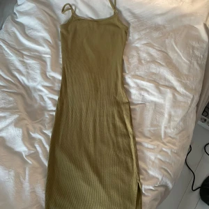 Beige ribbad långklänning - Säljer en superfin olivgrön ribbad långklänning. Den är ärmlös med smala axelband och har en slits längst ner. Perfekt för både vardag och fest! 💫