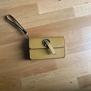 Axelremsväska  - Senapsgul-ish axelremsväska från NYPD. Kommer även med band ifall man vill förlänga väskan så att de blir en axelremsväska. 