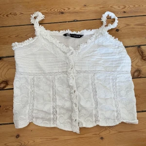 Vit spetslinne från Zara - Säljer ett superfint vitt linne från Zara som inte säljs längre i storlek xs. Linnet har spetsdetaljer och knappar framtill. Perfekt för sommardagar eller en festlig kväll! Sista bilden är lånad 