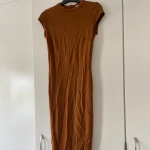 Brun klänning från H&M - Säljer en snygg brun klänning från H&M i storlek 36. Klänningen är lång och har en slits baktill för extra rörelsefrihet, denna går även själv att justera till den längd man vill ha. Den är ärmlös och har en tight passform som framhäver figuren. Perfekt för både vardag och fest!
