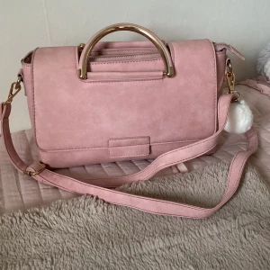 rosa väska i mocka imitation  - Rosa väska med mocka imitation, väskan är rymlig, har ett stort fack och två små, lätt att öppna och stänga.