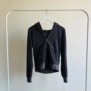 Mörkgrå hoodie från Juicy Couture - Säljer en snygg mörkgrå hoodie från Juicy Couture. Den har en dragkedja framtill och en stor, glittrig JC-logga på ryggen. Hoodien är i mjukt material och har långa ärmar. Perfekt för en avslappnad stil!