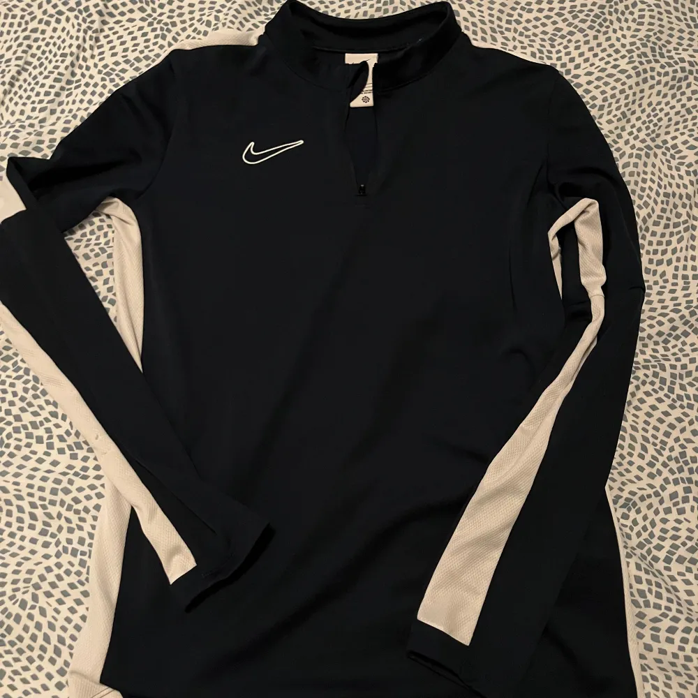 Säljer en mörkblå långärmad tröja från Nike med vita detaljer längs ärmarna. Tröjan är i Dri-FIT-material vilket gör den perfekt för träning. Den har en dragkedja vid halsen och är i storlek XL. Men passar S Perfekt för höst- och vinterträning!. Tröjor & Koftor.