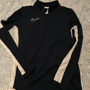 Mörkblå långärmad tröja från Nike - Säljer en mörkblå långärmad tröja från Nike med vita detaljer längs ärmarna. Tröjan är i Dri-FIT-material vilket gör den perfekt för träning. Den har en dragkedja vid halsen och är i storlek XL. Men passar S Perfekt för höst- och vinterträning!