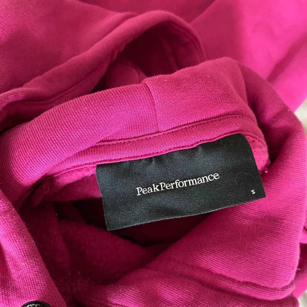 Säljer en snygg och bekväm rosa hoodie från Peak Performance. Den har en klassisk design med en stor ficka fram och justerbar huva. Perfekt för både vardag och chill. Peak Performance-loggan är broderad på framsidan. Passar perfekt för höst och vår!. Tröjor & Koftor.