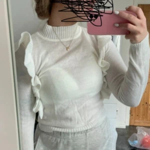 Vit tröja med volangdetaljer - Säljer en superfin vit tröja med volangdetaljer längs ärmarna. Den är långärmad och har en ribbad krage samt muddar vid ärmslut och nederkant. Perfekt för både vardag och fest! 🕊️