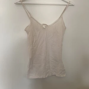 Vit linnetopp från H&M - Säljer en enkel och stilren vit linnetopp från H&M Basics. Den är ärmlös med smala axelband och perfekt för sommardagar. Toppen är i storlek XS och passar bra till både vardag och fest.