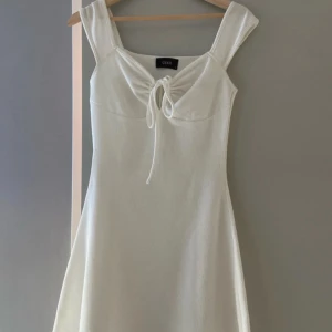 Vit klänning med knyt från Cider - Snygg vit student klänning från Cider v-ringad med knyt framtill och breda axelband som gör att de inte glider ner. Perfekt för sommarens alla tillfällen. Den ger en smickrande passform och är tillverkad i ett mjukt stretchigt material. Använd endast en gång, hör av dig om du har någon fråga ✨🙌