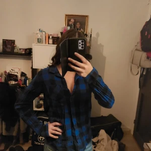 Blå och svart rutig skjorta - Snygg blå och svart rutig skjorta med långa ärmar. Perfekt för en avslappnad stil. Skjortan har en klassisk krage och knappar framtill.