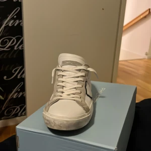 Vita sneakers från Philippe Model - Snygga vita sneakers från Philippe Model med grå och svarta detaljer. Skorna har klassisk snörning och en stilren design som passar perfekt till vardags. De är märkta med logotypen på sidan och baksidan.