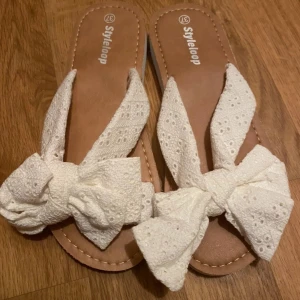 Vita sandaler med rosett från Styleloop - Charmiga vita sandaler från Styleloop med en stor rosett på ovansidan. Perfekta för sommardagar, dessa sandaler har en bekväm sula och ett stilrent utseende.