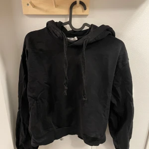 Svart hoodie från NA-KD - Säljer en svart hoodie från NA-KD med justerbar huva och långa ärmar. Perfekt för en avslappnad stil. Den har en klassisk design med ribbade muddar och nederkant.