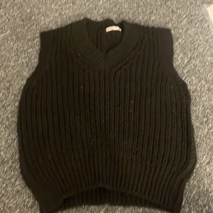 Svart stickad väst - Säljer en svart stickad väst med v-ringad design. Perfekt för lager-på-lager och ger en stilren look. Passar bra till både vardag och mer uppklädda tillfällen.