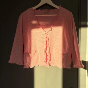 Rosa kofta med volangdetaljer - Söt rosa kofta med volangdetaljer längs kanten och trekvartsärmar från Cellbes.💗 Står storlek (42)/(44) men skulle säga att den passar (L)-(M) i storlek.🥰