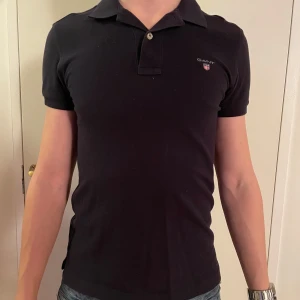 Mörkblå pikétröja från GANT - Snygg mörkblå pikétröja från GANT i slim fit och i storlek XS. Personen på bilden är 177 cm lång och väger 65 kg. Nypris är ca 600 kr. Tröjan är i bra skick och använd ett fåtal gånger. Hör av dig vid frågor!