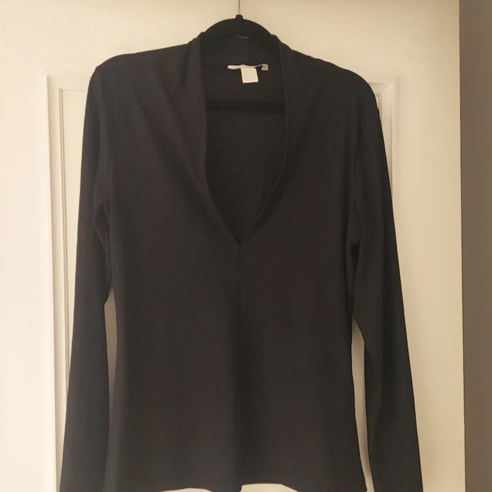 Säljer en stilren svart långärmad tröja med v-ringning. Perfekt för en minimalistisk look och passar bra till både jeans och kjol. Ett mångsidigt plagg för garderoben.. Neuletakit & Villapaidat.