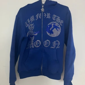 Blå hoodie med dragkedja och tryck - Snygg blå hoodie från Aim for the Moon med dragkedja och ett coolt tryck på framsidan. Perfekt för en avslappnad stil. Hoodien har långa ärmar och en bekväm passform.