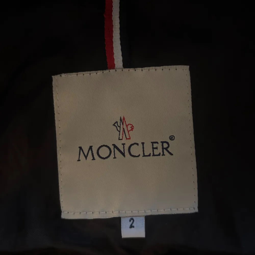 Snygg svart dunväst från Moncler med pälsdetaljer på huvan och dragkedja vid fickorna.. Takit.