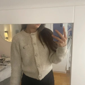 Beige stickad kofta med knappar - Mysig beige stickad kofta med  knappar. Perfekt för kyliga dagar och ger en stilren look. Koftan har en klassisk design med rund hals och långa ärmar. Stolelk xs