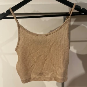 Beige glittrig linnetopp - Snygg beige glittrig linnetopp med smala axelband. Perfekt för en kväll ute eller en festlig tillställning. Toppen är croppad och har en stilren design som passar till många olika outfits.