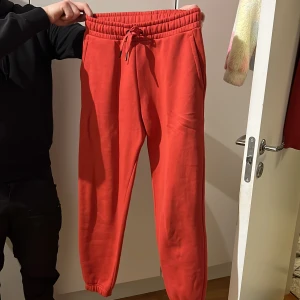 Röda mjukisbyxor från Peak Performance - Snygga röda mjukisbyxor från Peak Performance med elastisk midja och snörning. Byxorna har en bakficka och är perfekta för en avslappnad stil. De är tillverkade i ett mjukt material som ger en bekväm passform.