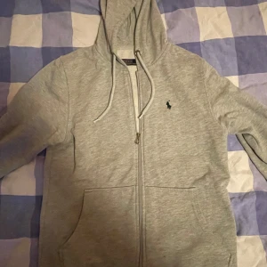 Grå hoodie från Polo Ralph Lauren - Säljer en stilren grå hoodie från Polo Ralph Lauren. Den har en dragkedja framtill och en klassisk logga på bröstet. Perfekt för en avslappnad stil. Skick 10/10 knappt använd size M